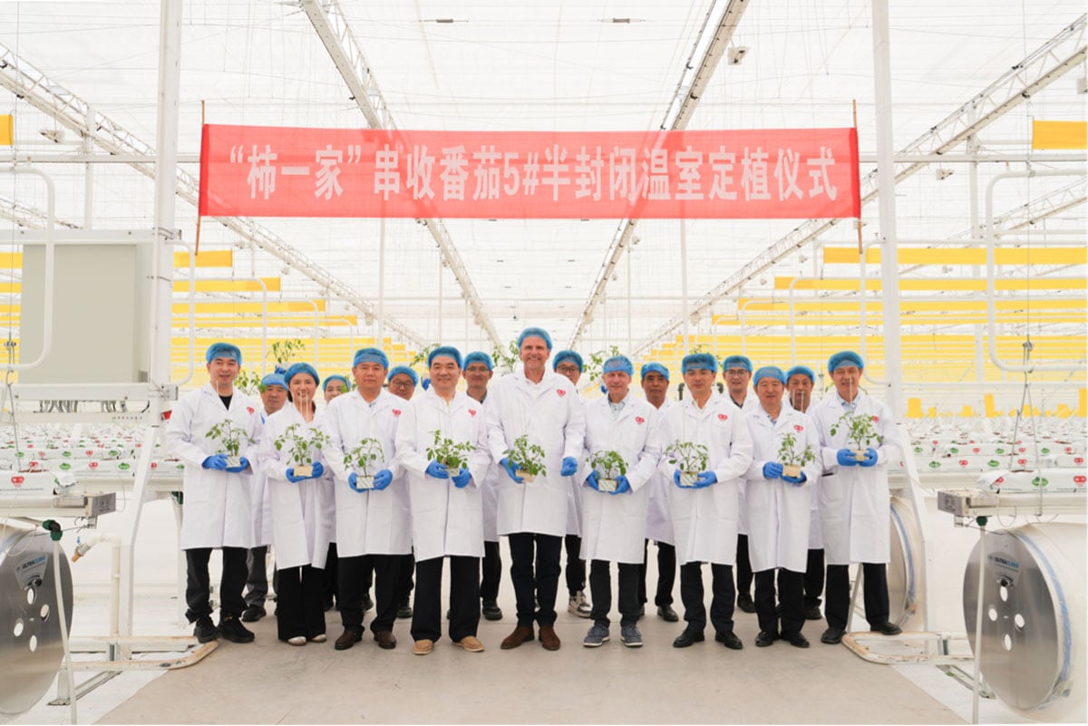 A group of individuals in lab coats and hats, standing in front of a large banner with Chinese characters, indicating a scientific or industrial setting.